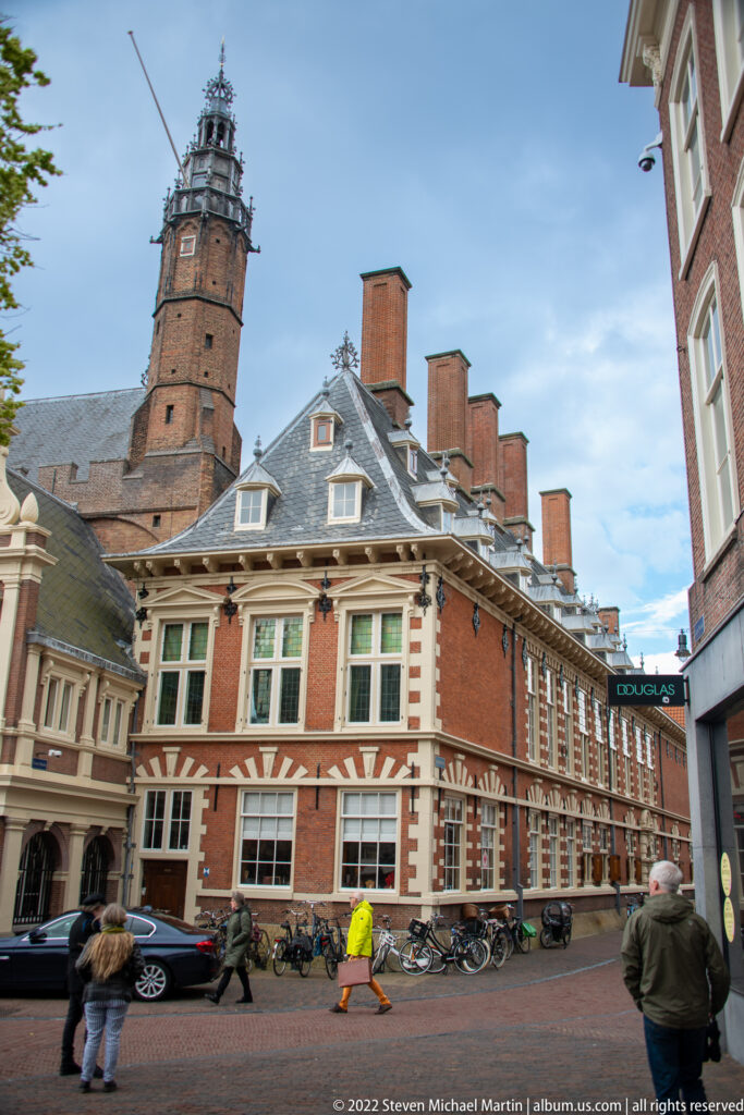 Long red-brick civic building with white stone trim, steep roof, and square tower, with bicycles along the street.