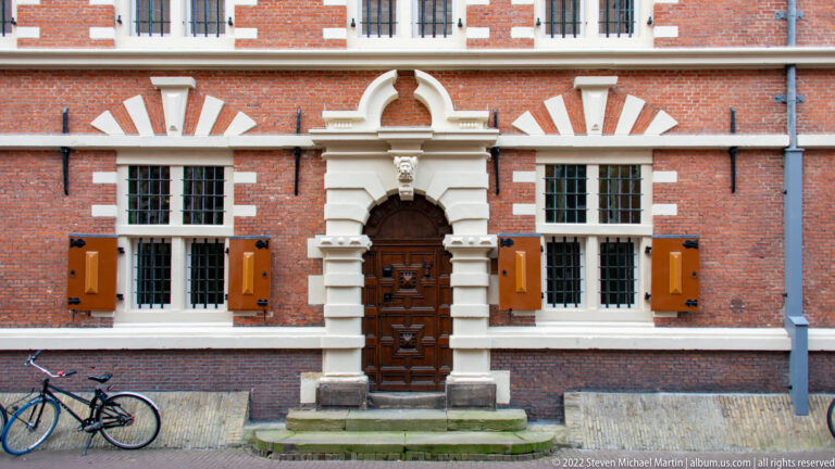 Ornate carved stone doorway with dark wooden door centered in a red-brick façade with white-trimmed windows.