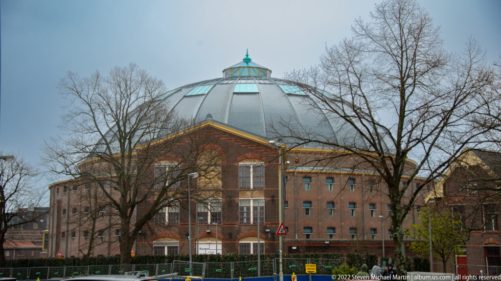 Large domed brick building of the former Koepelgevangenis in Haarlem, partly screened by leafless trees.