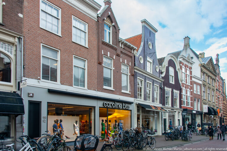 Row of narrow historic gabled buildings with modern shops and many bicycles along a busy Haarlem street.