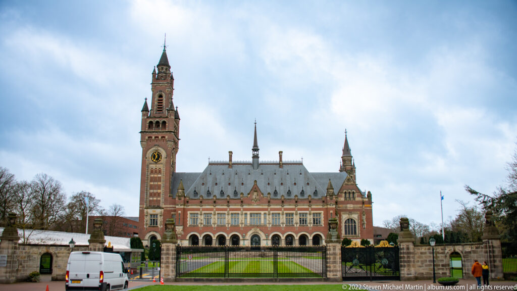 Peace Palace in The Hague with tall clock tower, red-brick façade, slate roof, lawn, and perimeter gate.