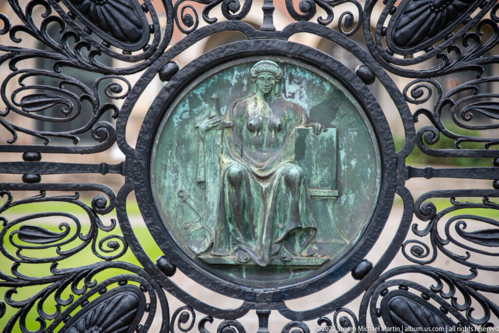 Circular green-patinated bronze relief of a seated female figure within black scrollwork on the Peace Palace gate.