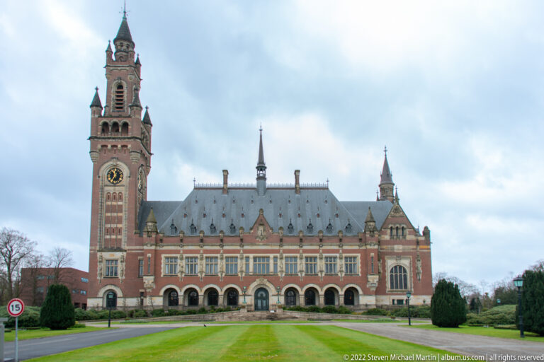 Peace Palace façade across a green lawn, with clock tower at left and arched ground-floor openings.