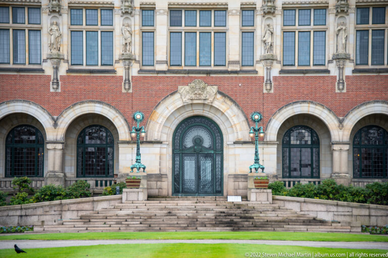 Arched Peace Palace doorway reached by steps, flanked by turquoise lamps beneath tall windows and stone sculpture.