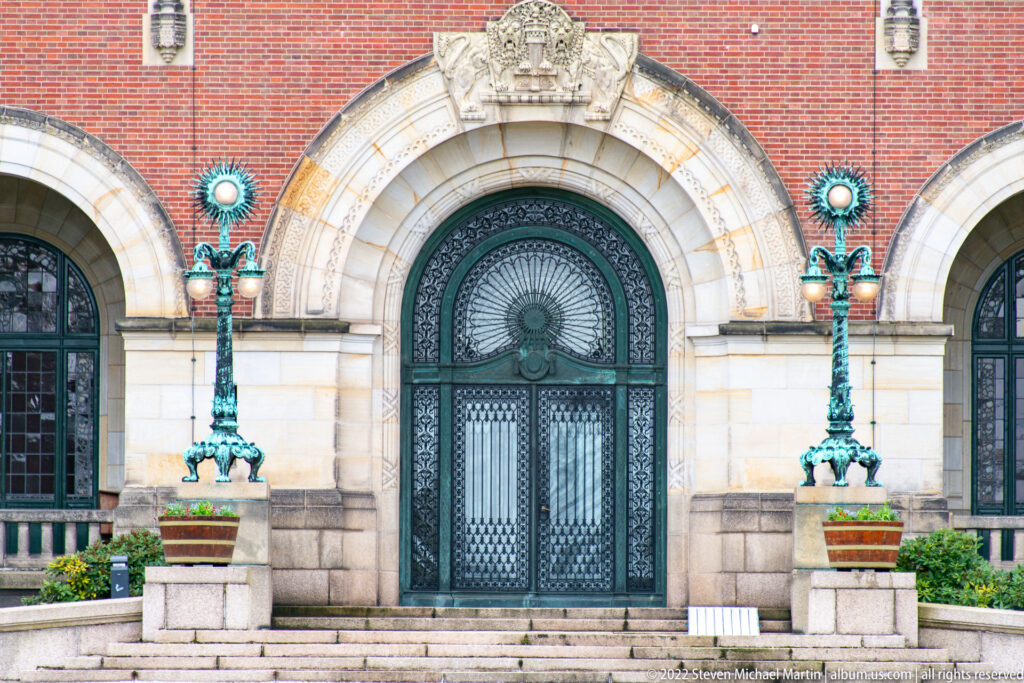 Close view of the Peace Palace arched metal doorway with paired green-patinated lamps and carved stone surround.