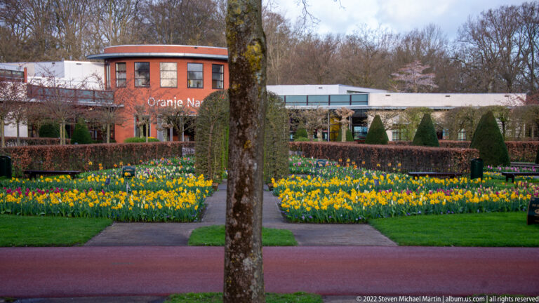 Oranje Nassau pavilion behind geometric yellow-and-white flower beds, divided by straight paths and a central tree trunk.