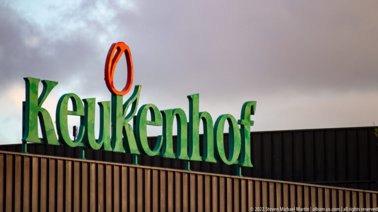 Large green Keukenhof rooftop sign with orange tulip emblem against a gray sky.