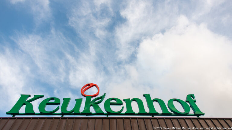 Green Keukenhof roof sign and orange tulip emblem silhouetted beneath a broad cloudy sky.