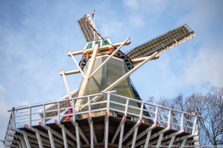 Low-angle view of the Keukenhof windmill’s upper body, white gallery, timber braces, and latticework sails.