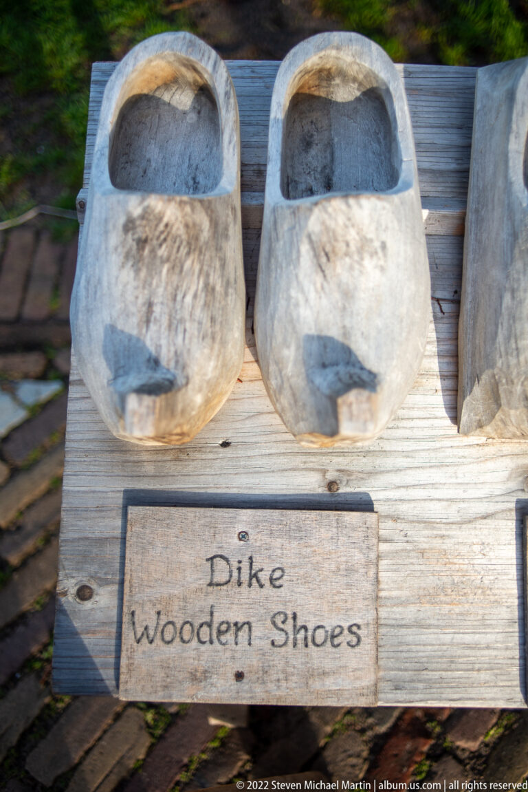 Pair of pale carved wooden shoes on a plank display above a sign reading “Dike Wooden Shoes.”