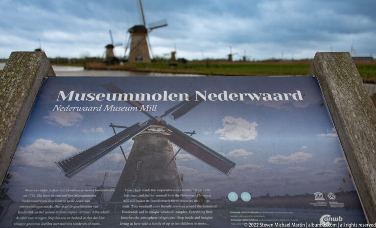 Interpretive panel titled Museummolen Nederwaard with a windmill visible beyond it across the water.