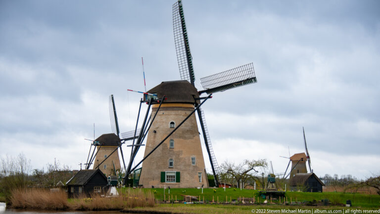 Three traditional windmills aligned across the polder, with a large brick mill in the foreground.