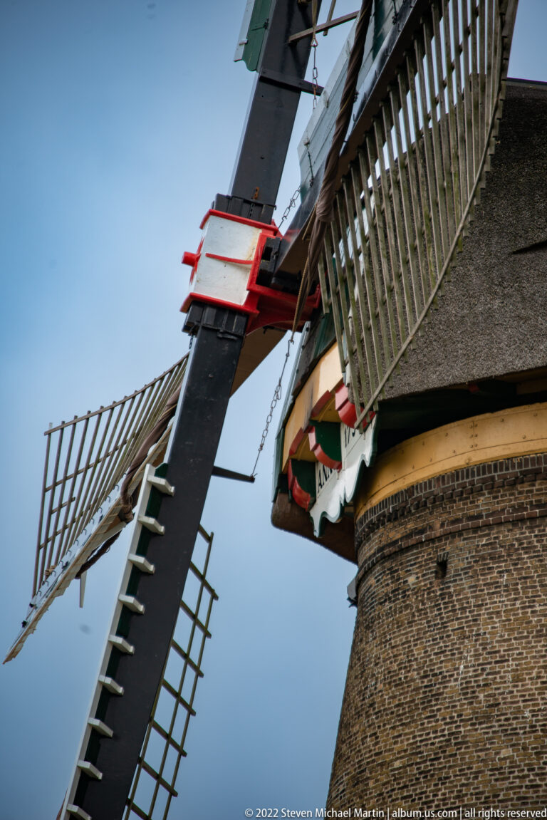 Close-up of windmill sails crossing beside a thatched cap and brick tower.