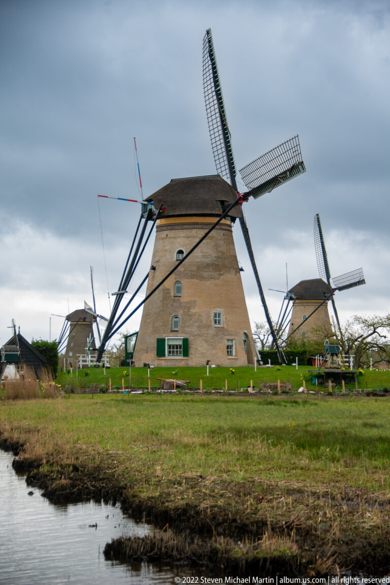 Large brick windmill centered between smaller neighboring mills, with a narrow drainage ditch in front.
