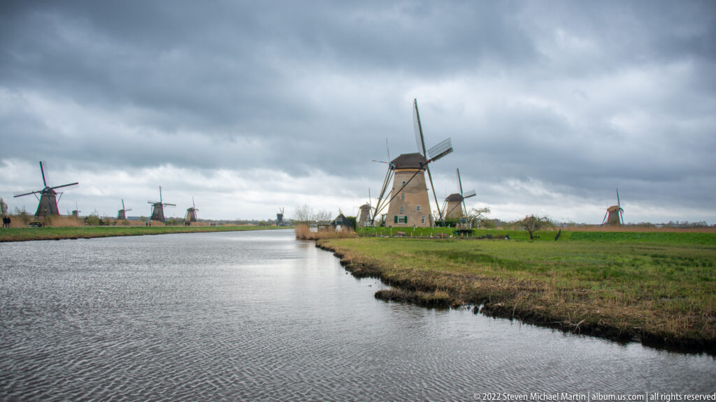 Long canal extending toward the horizon with windmills spaced along both sides.