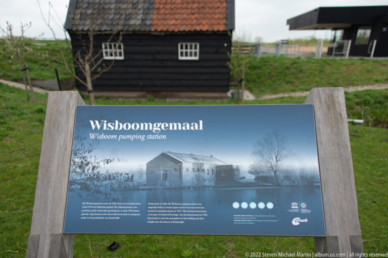 Interpretive panel titled Wisboomgemaal, Wisboom pumping station, with a dark building behind it.