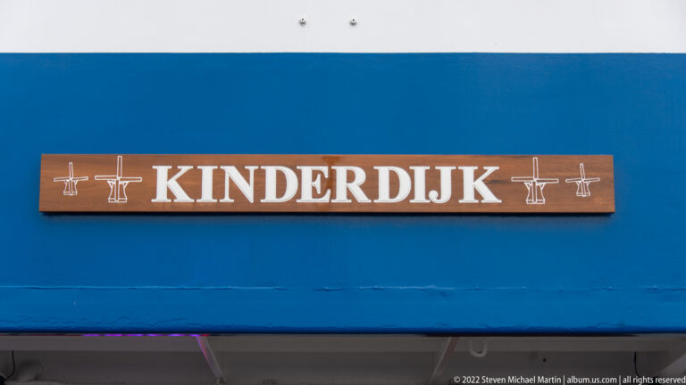 Wooden KINDERDIJK nameplate with small windmill motifs mounted on a bright blue vessel side.