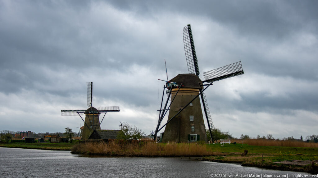 Two traditional windmills beside a broad waterway beneath dark overcast clouds.