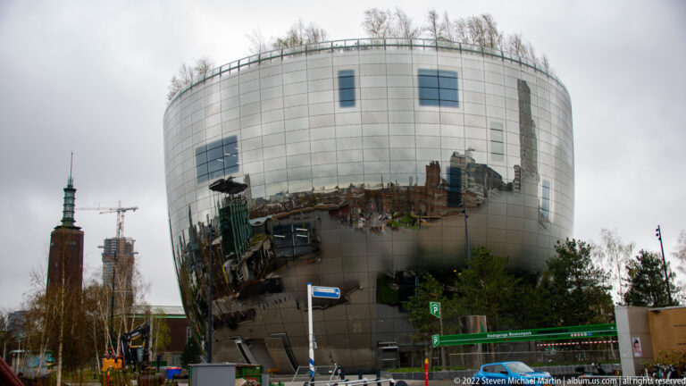 Mirrored bowl-shaped Depot Boijmans Van Beuningen reflecting Rotterdam streets and skyline beneath a planted rooftop edge.