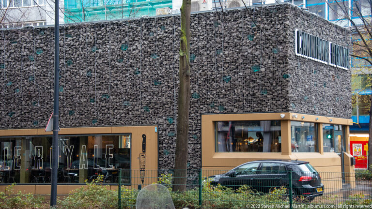 Low stone-filled gabion-clad commercial building with large windows and rooftop lunchroom lettering.