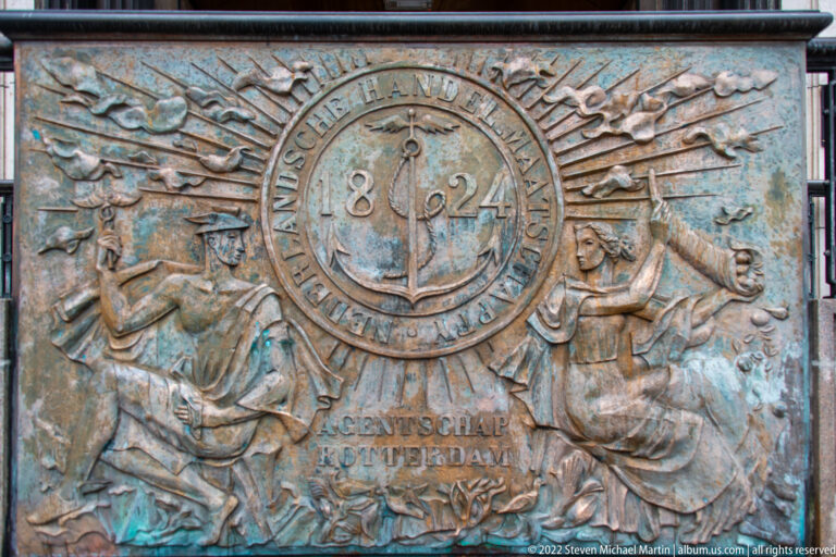 Weathered bronze relief with the date 1824 in a circular medallion, allegorical figures, Dutch text, and green patina.