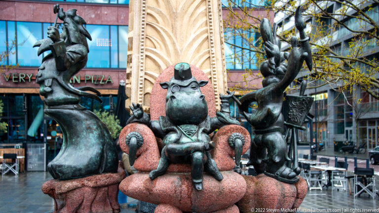 Three dark bronze whimsical animal-like figures arranged on a reddish stone base in a Rotterdam public monument.