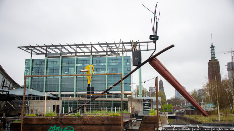 Abstract sculpture of long red, black, and yellow metal elements in front of a glass building in Rotterdam's Museumpark.