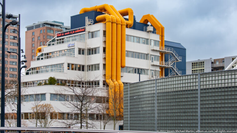 White multi-story building with enormous orange pipes wrapping over the roof and descending the façade.