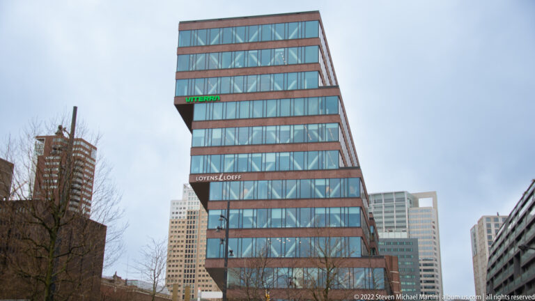 Leaning glass office tower with horizontal bands and Loyens & Loeff signage against Rotterdam high-rises.