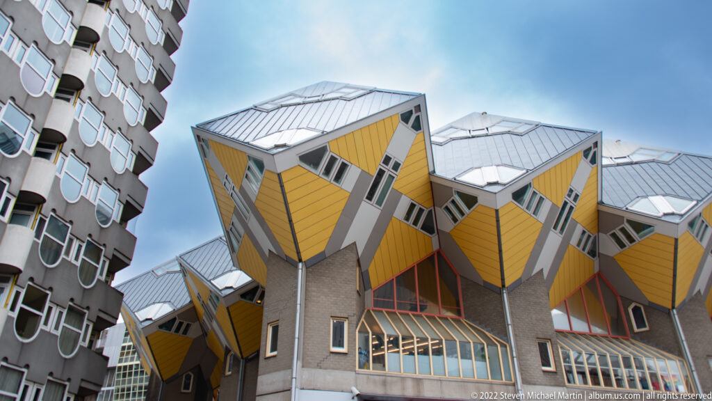 Yellow Rotterdam Cube Houses tilted on their corners above gray supports, with triangular windows and silver roofs.