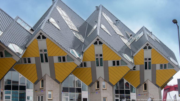 Four front-facing yellow Cube Houses with gray central bands, small windows, and steep silver roofs.