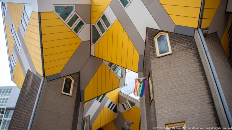 Upward view between Cube Houses showing yellow undersides, gray masonry support cores, small windows, and tight passage space.