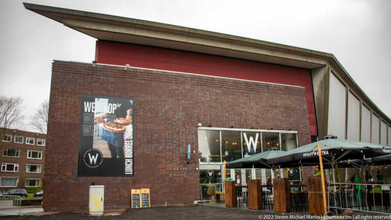 Brick cultural building with glass entrance, poster, and outdoor café seating in Rotterdam's Museumpark area.