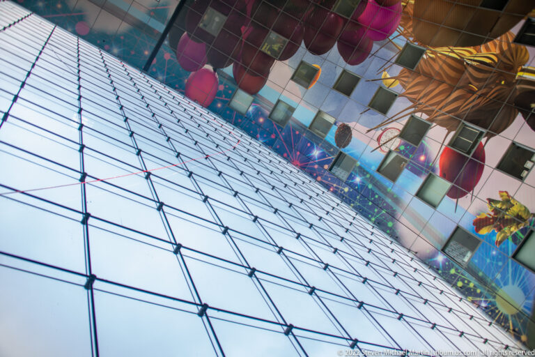 Diagonal interior view of Markthal showing the gridded glass end wall below a ceiling covered with oversized colorful food imagery.