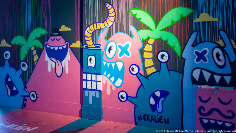 Colorful cartoon monster mural with pink and blue creatures, palms, striped background, and the tag #KRALEN near the bottom.