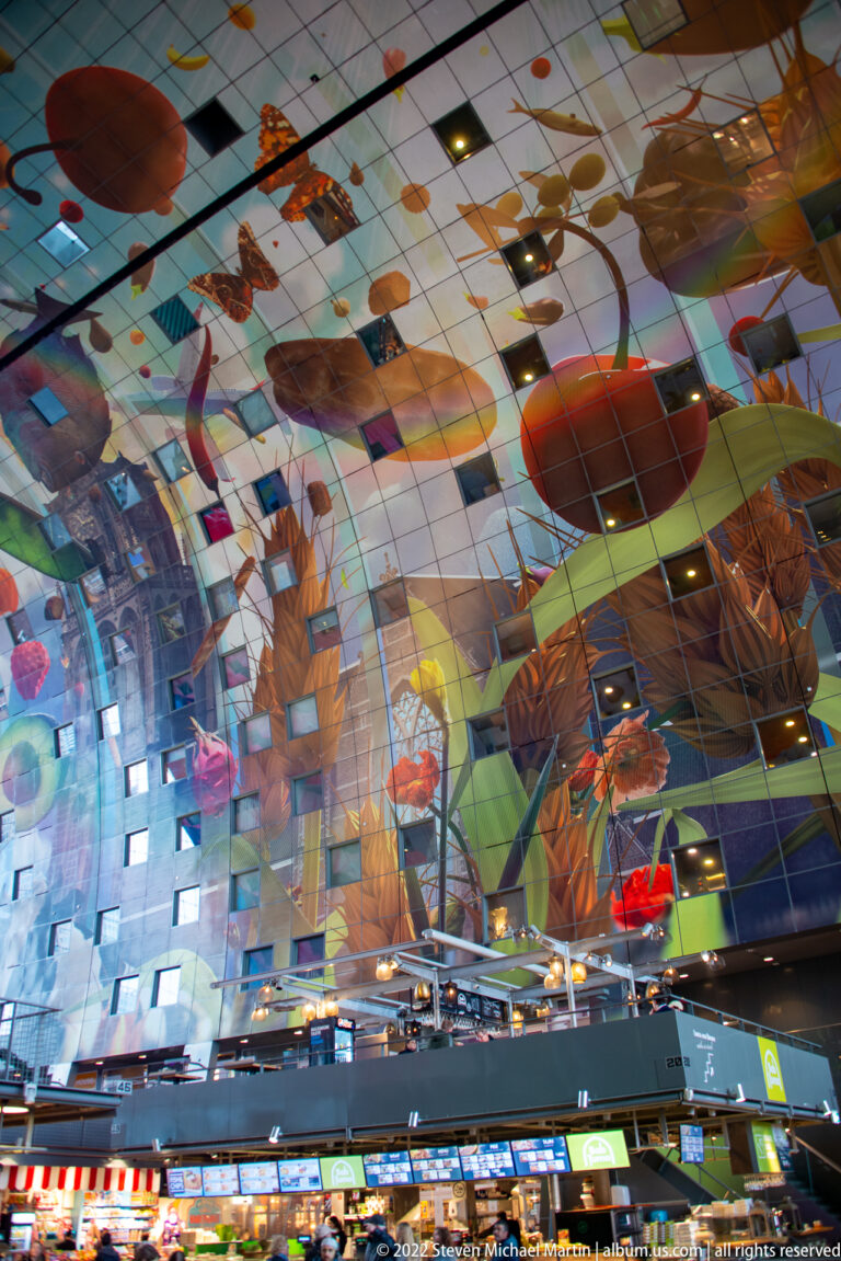 Wide Markthal interior with giant colorful food imagery covering the curved ceiling above market stalls and visitors.