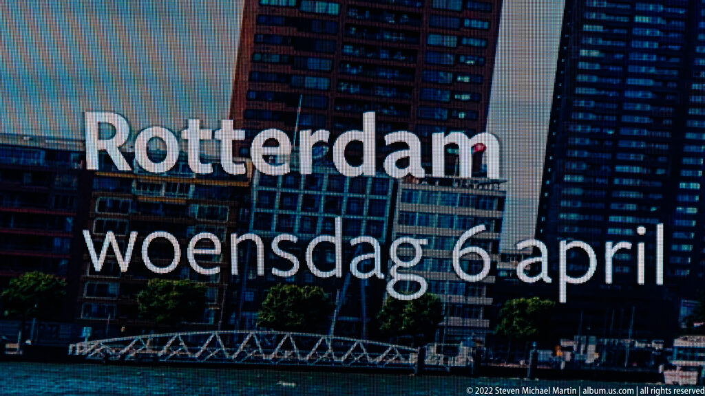 White text reading Rotterdam woensdag 6 april across a transparent surface with apartment buildings visible behind.