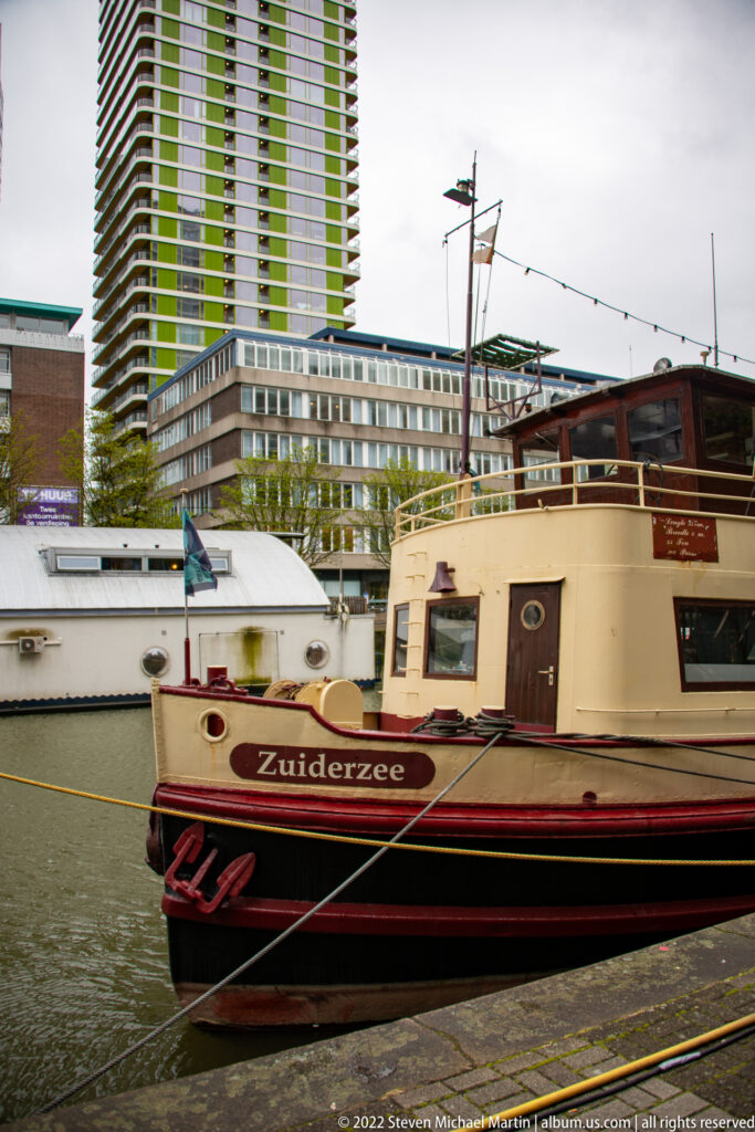 Cream-and-dark-hulled vessel named Zuiderzee moored beside a quay, with modern high-rise buildings behind.