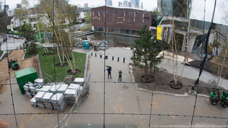 Curved mirrored façade reflecting trees, pedestrians, construction materials, and service vehicles in Museumpark.