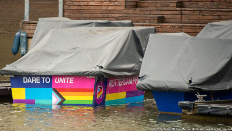 Covered small boats beside a rainbow-colored floating display reading DARE TO UNITE and Rotterdam.