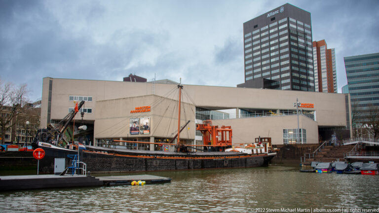 Historic vessel moored on the water in front of the Maritime Museum Rotterdam building and nearby office towers.
