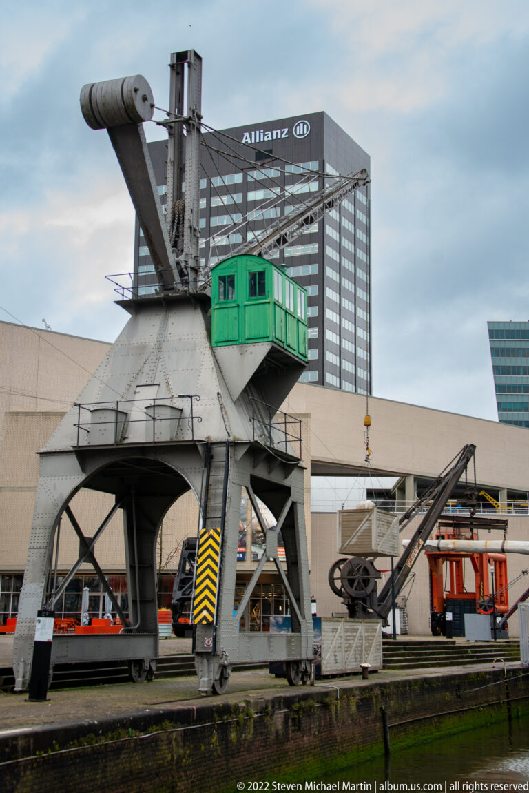 Close view of a gray steel harbor crane with green operator’s cab, pulleys, braces, and lifting machinery.