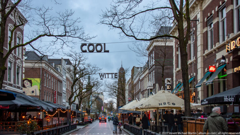 Witte de Withstraat lined with brick buildings, restaurants, awnings, outdoor seating, traffic, and suspended street lettering.