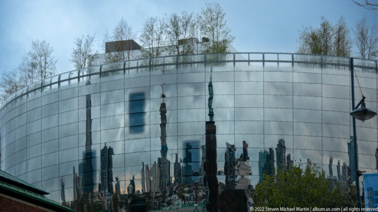 Curved mirrored façade of Depot Boijmans Van Beuningen reflecting Rotterdam towers, trees, and lampposts.