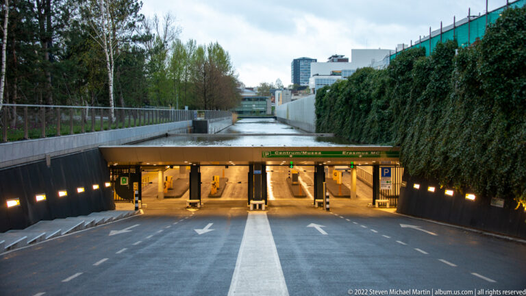 Roadway ramp descending to an underground Museumpark parking entrance with lit booths, arrows, and planted walls.