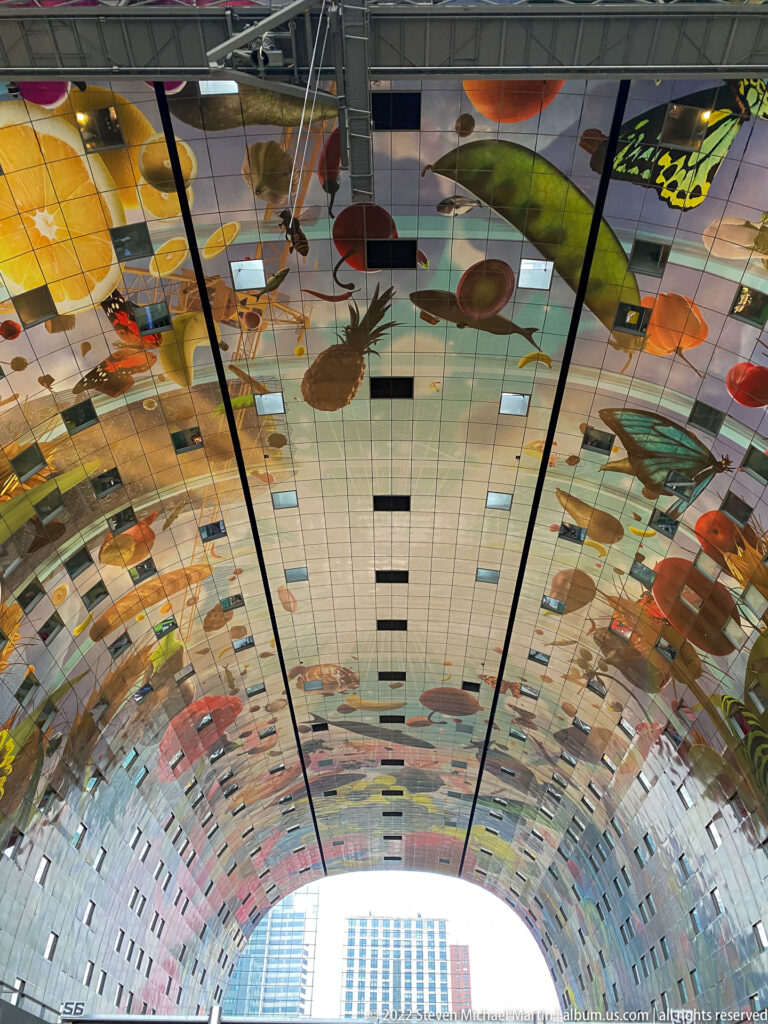 Curving Markthal ceiling covered with oversized colorful food imagery and panel seams above the market hall.