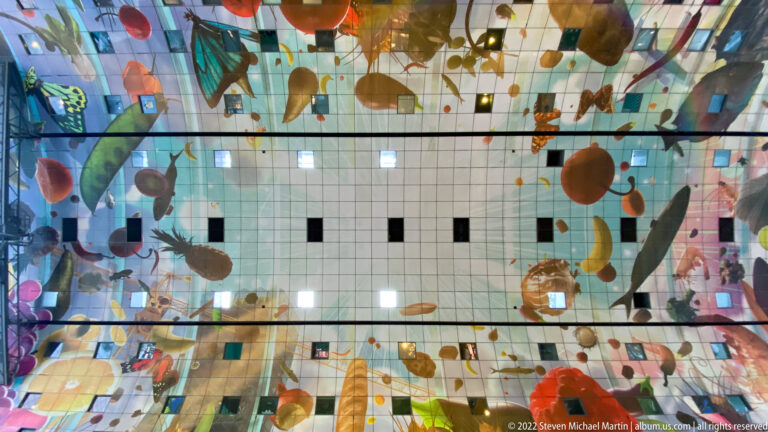 Upward view of Rotterdam Markthal ceiling with oversized colorful food forms arranged across a gridded curved surface.