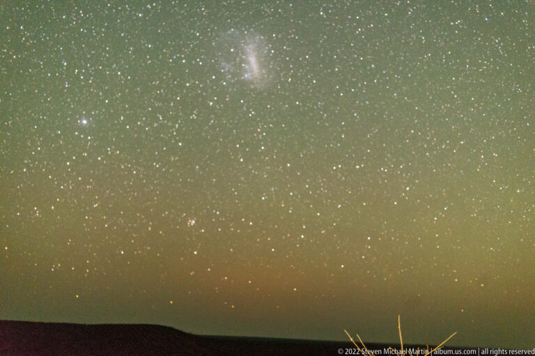 Star-filled southern sky with a diffuse luminous cloud above a low dark horizon.