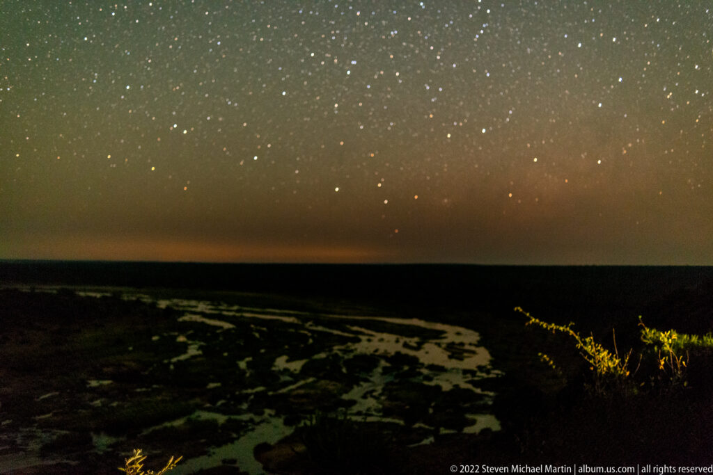 Star-filled night sky above pale winding channels of the Olifants River floodplain and a dark horizon.