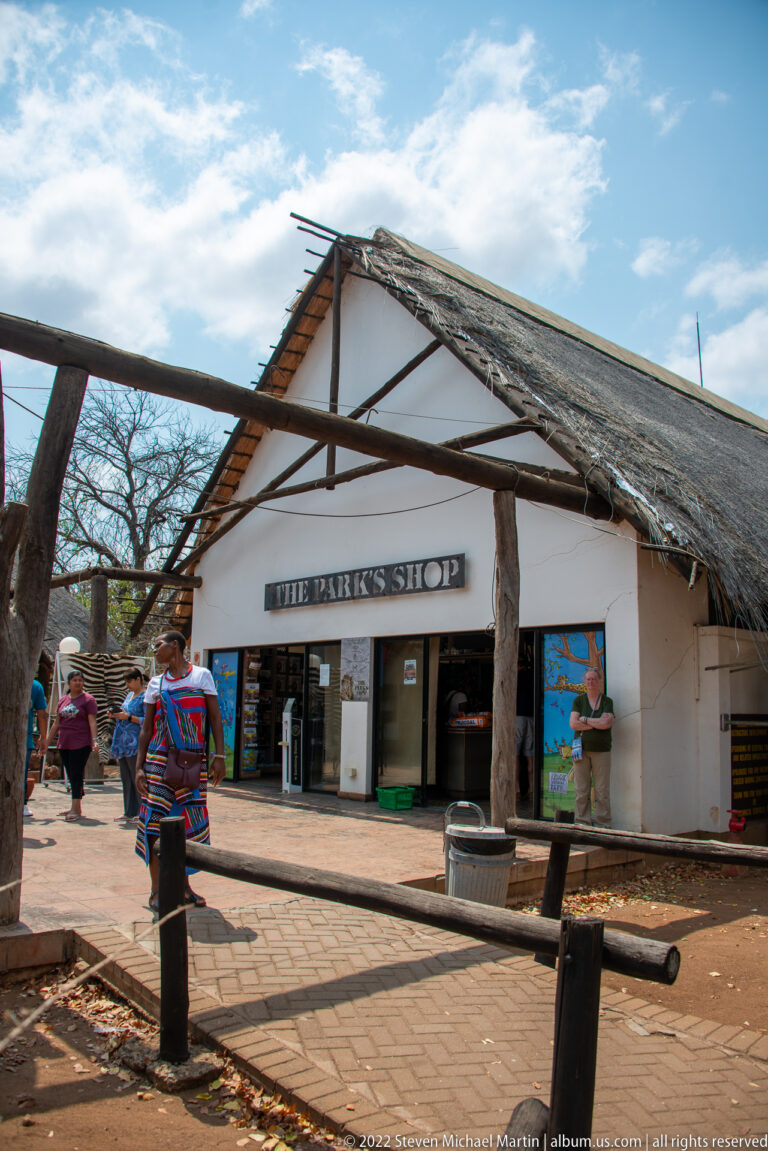 White park shop building with a broad thatched roof, timber supports, entrance displays, and visitors outside.